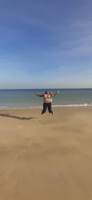 Jeune fille qui saute dans le sable devant une plage.